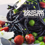 Close up portrait image of a tall pine of squid ink spaghetti on a white plate served with peas, pepperoni and parmesan cheese shavings with text