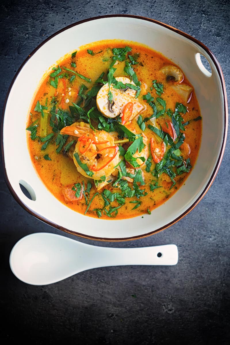 Portrait overhead image of a Tom Yum Soup served in an Asian style soup bowl decorated with a blue flower in a dark setting