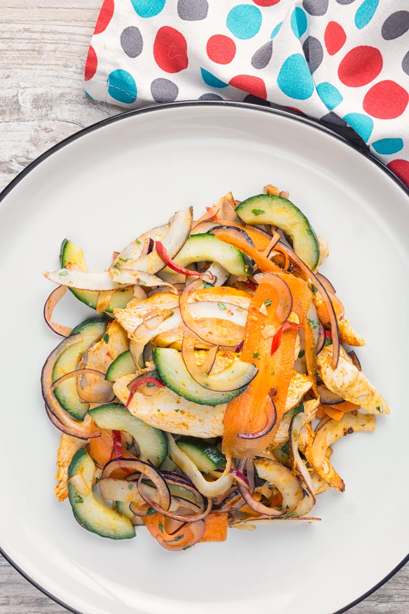 Overhead portrait image of a Thai salad featuring chicken breast, fresh coconut, carrots and red onion