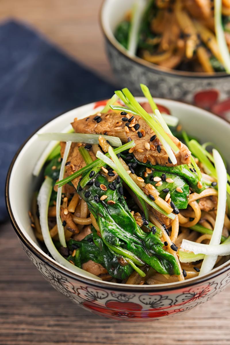 Portrait overhead image of a pork stir fry with spinach and noodles served an Asian style bowl