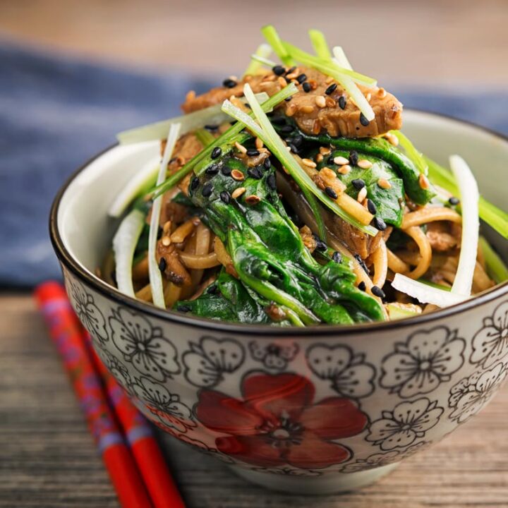 Portrait image of a pork stir fry with spinach and noodles served an Asian style bowl decorated with a red flower