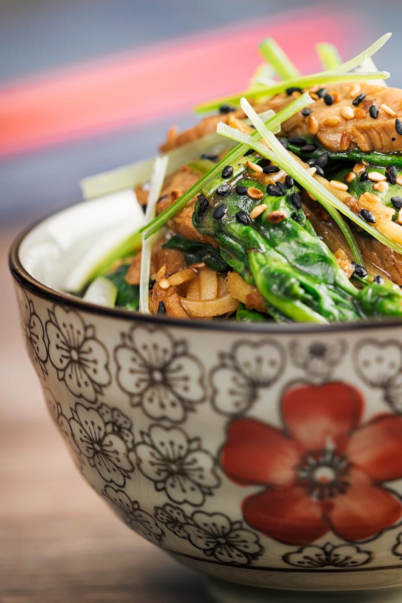 Portrait close up image of a pork stir fry with spinach and noodles served an Asian style bowl decorated with a red flower