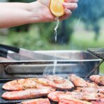 Portrait image of fresh lemon being squeezed over BBQ prawns or shrimp on a BBQ with watermelon