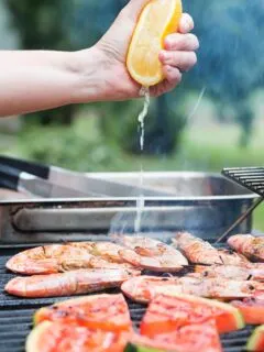 Portrait image of fresh lemon being squeezed over BBQ prawns or shrimp on a BBQ with watermelon