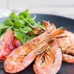 Portrait image of large BBQ prawns or shrimp with grilled watermelon served on a black plate