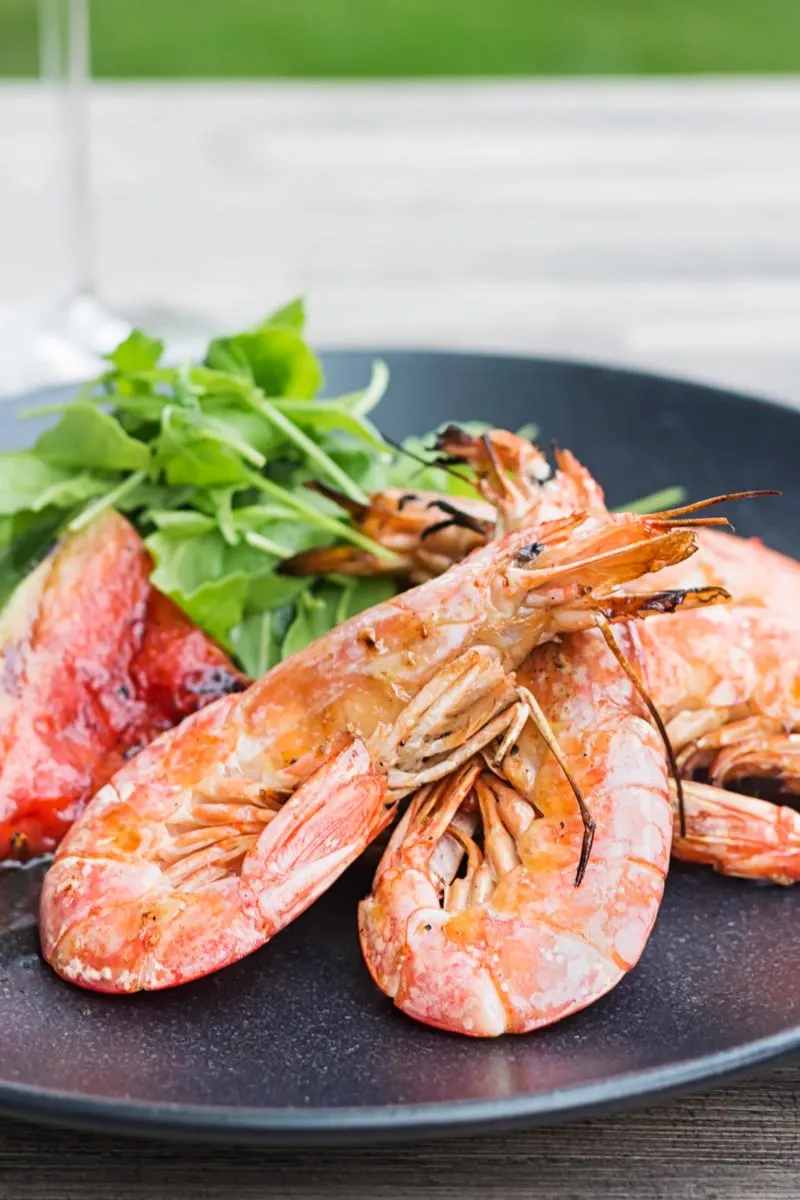 Portrait image of large BBQ prawns or shrimp with grilled watermelon served on a black plate
