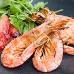 Portrait close up image of large BBQ prawns or shrimp with grilled watermelon served on a black plate