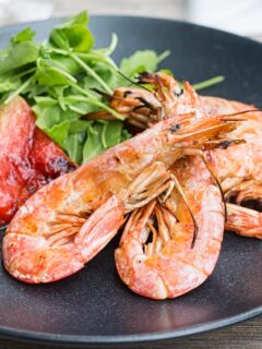 Portrait close up image of large BBQ prawns or shrimp with grilled watermelon served on a black plate