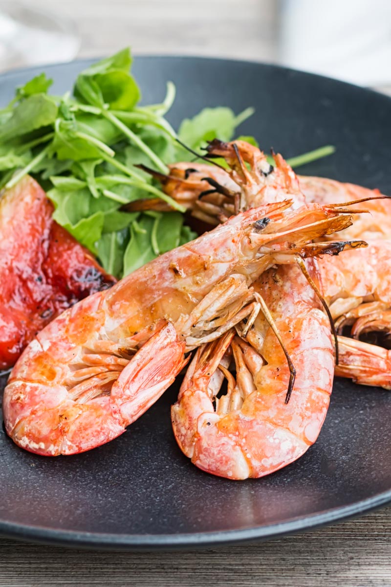 Portrait close up image of large BBQ prawns or shrimp with grilled watermelon served on a black plate