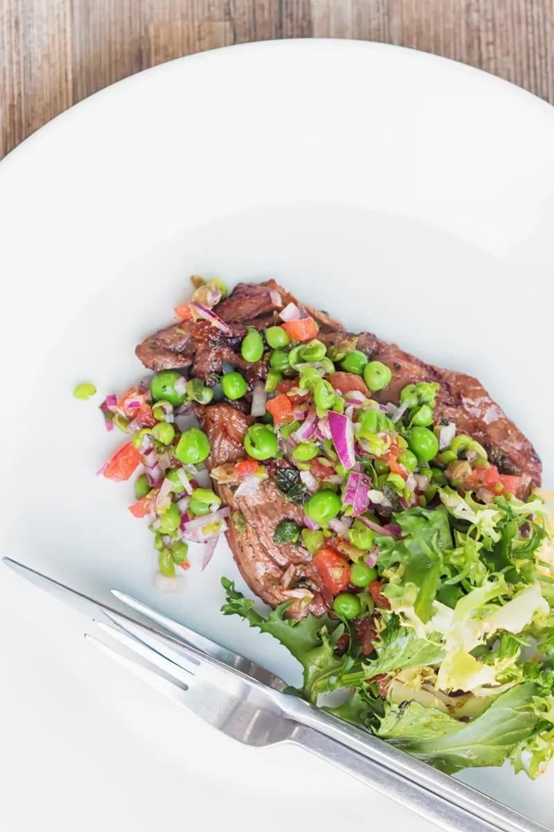 Portrait overhead image of a minted pea salsa served with lamb and a side salad on a white plate