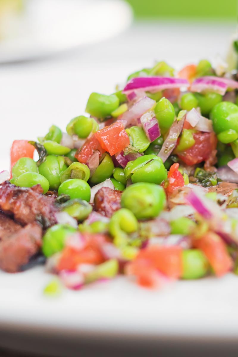 Close up portrait image of a minted pea salsa served with lamb and a side salad on a white plate