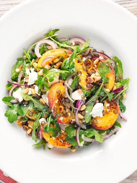 Portrait overhead image of a seared peach and feta cheese salad with rocket, puy lentils and toasted pine nuts served in a white bowl