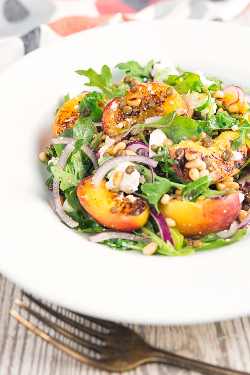 Portrait image of a seared peach and feta cheese salad with rocket, puy lentils and toasted pine nuts served in a white bowl