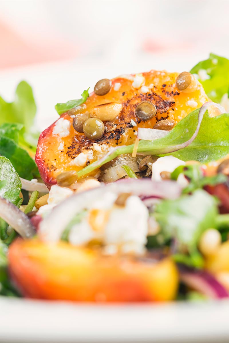 Portrait close up image of a seared peach and feta cheese salad with rocket, puy lentils and toasted pine nuts served in a white bowl