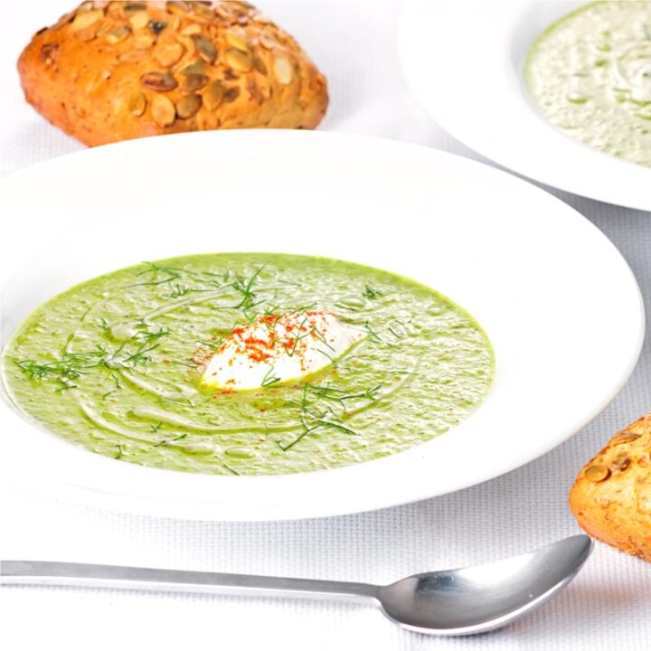 Square image of a sorrel and fennel soup served in a white bowl with a dollop of sour cream and sprinkling of paprika