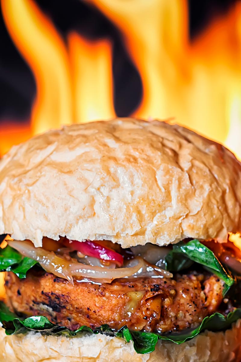 Portrait close up image of a vegetable burger topped with an onion and peach chutney served on a bun with a flaming background