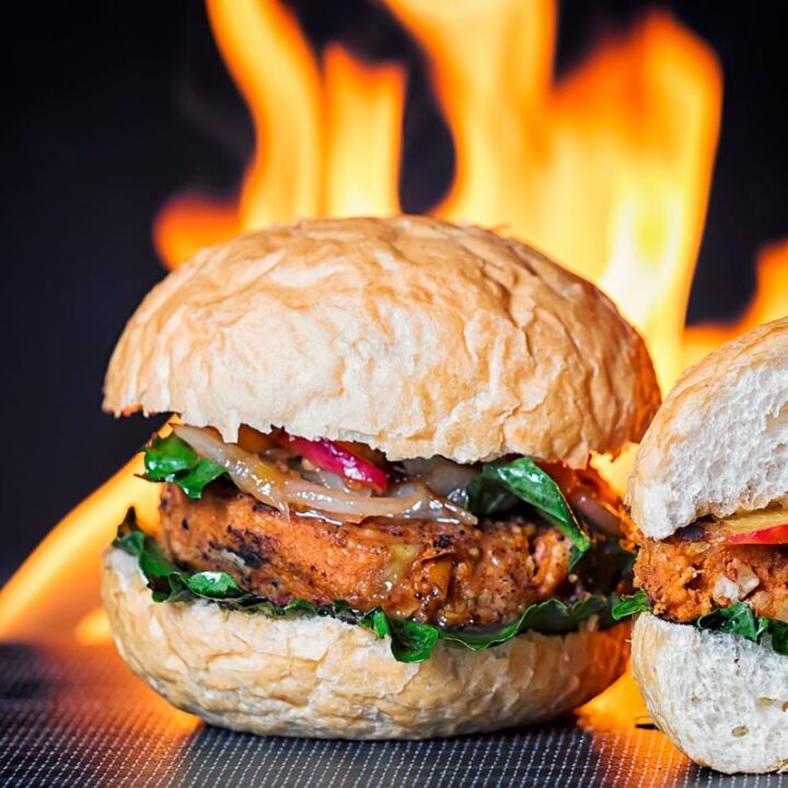 Square image of a spicy bean burger topped with an onion and peach chutney served on a burger bun with a flaming background