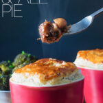 Portrait image of a beef and ale pie served pot pie style in a red pot with a fork removing steaming pie filling with text overlay