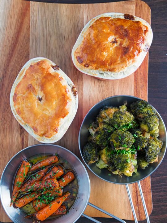 Portrait over head image of two beef and ale pies served pot pie style with glazed carrots and broccoli