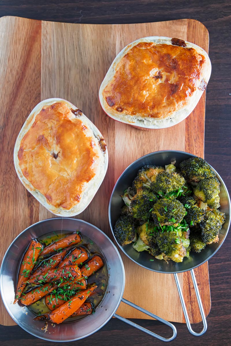 Portrait over head image of two beef and ale pies served pot pie style with glazed carrots and broccoli