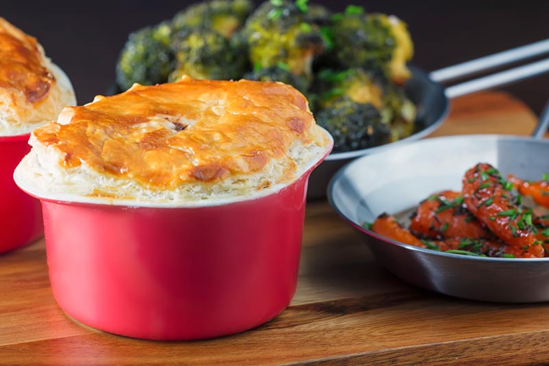 Landscape image of a beef and ale pie served pot pie style in a red pot