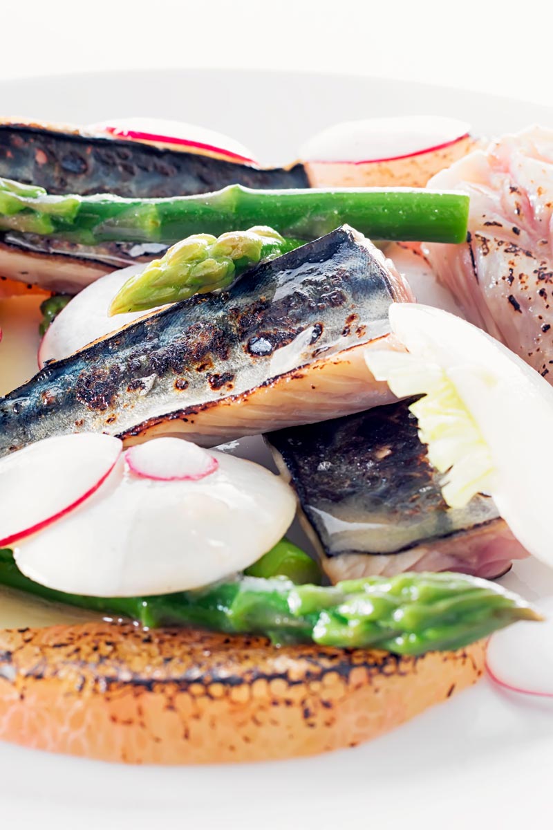 Portrait close up image of cured mackerel served in a salad featuring asparagus spears and pomelo