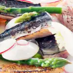 Portrait close up image of cured mackerel served in a salad featuring asparagus spears and pomelo with text