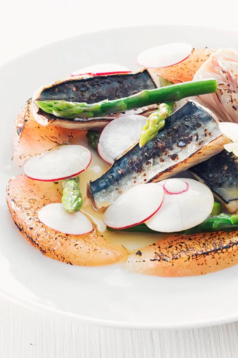 Portrait image of cured mackerel served in a salad featuring asparagus spears and pomelo