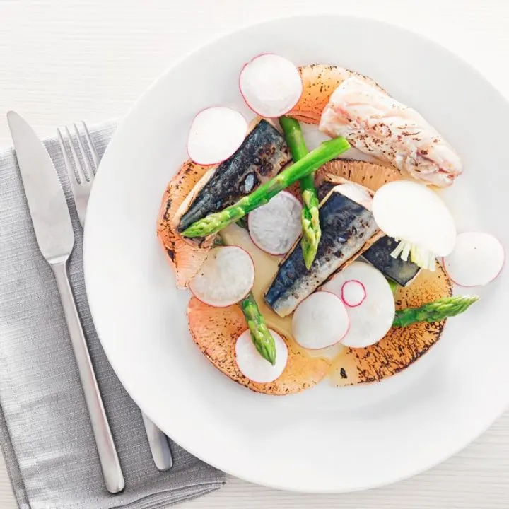 Square overhead image of cured mackerel served in a salad featuring asparagus spears and pomelo