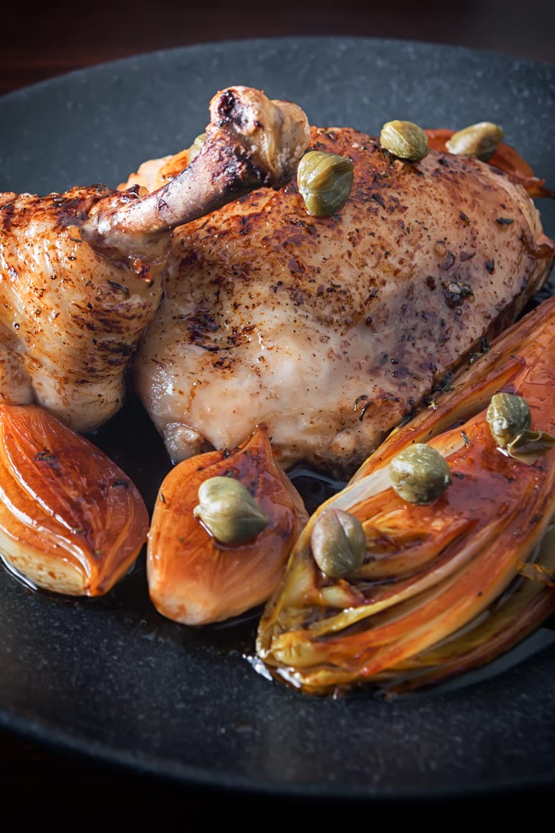 Portrait image of braised chicken legs served with Belgian Endive, shallots and capers on a black plate