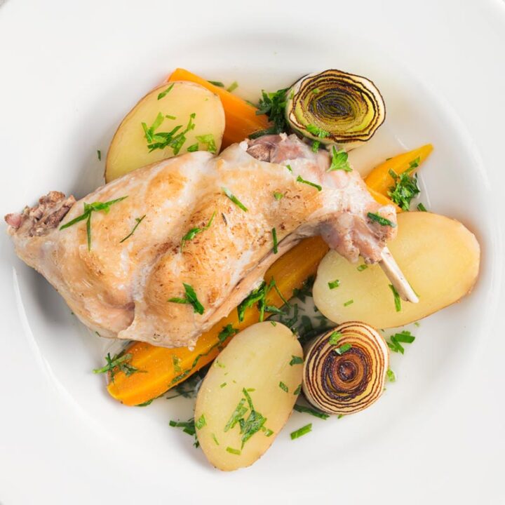 Square over head image of a braised rabbit leg served with new potatoes, carrots and seared leeks