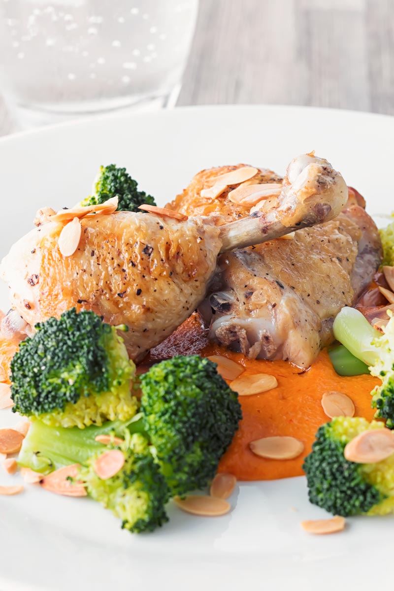 Portrait close up image of roast chicken legs served on a romesco sauce with steamed broccoli