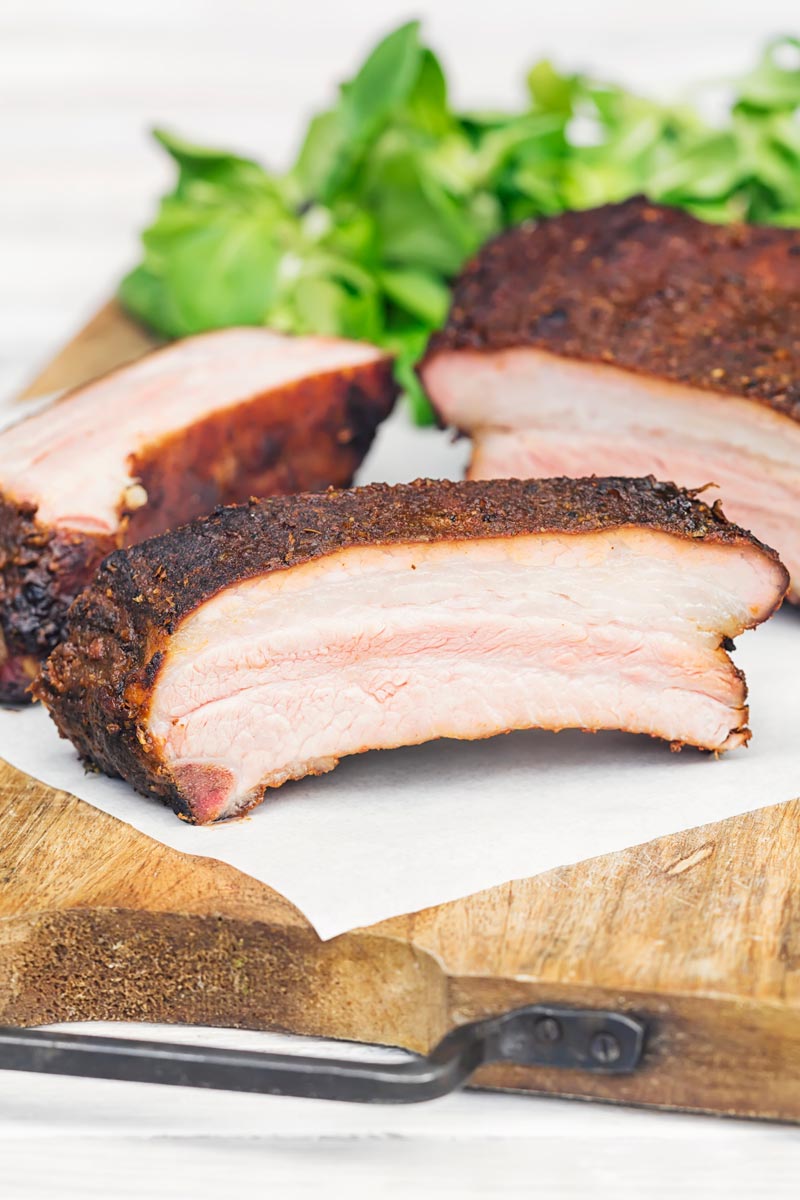 Portrait image of sliced smoked BBQ Ribs served on a chopping board with salad leaves