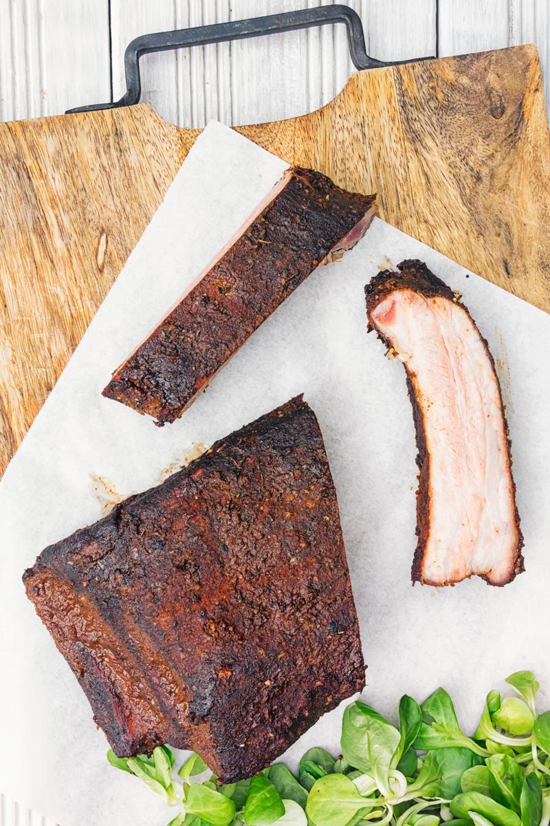 Portrait overhead image of sliced smoked BBQ Ribs served on a chopping board with salad leaves