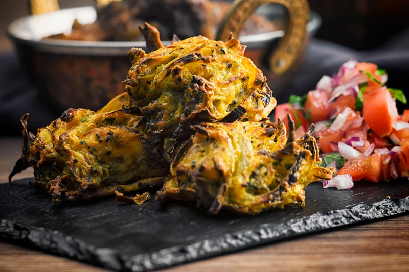 Landscape image of onion bhaji pakora served with a tomato salad on a slate