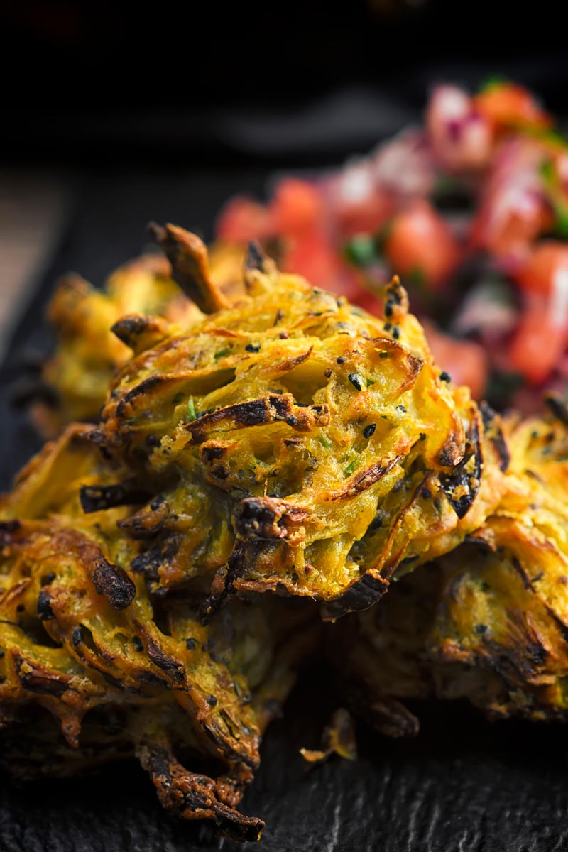 Portrait close up image of onion bhaji pakora served on a slate with a tomato salad