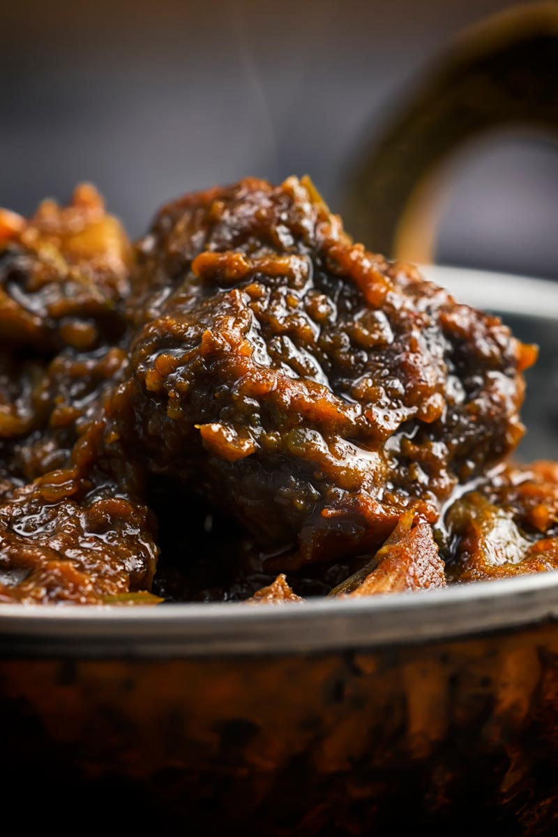 Close up portrait image of a pork vindaloo curry served in a copper curry bowl