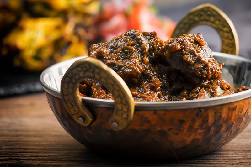 Landscape image of a pork vindaloo curry served in a copper curry bowl