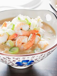 Landscape close up image of a chicken and prawn soup served in an Asian style bowl decorated with a blue flower
