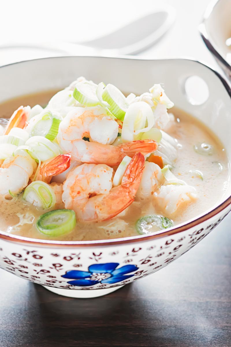 Landscape close up image of a chicken and prawn soup served in an Asian style bowl decorated with a blue flower
