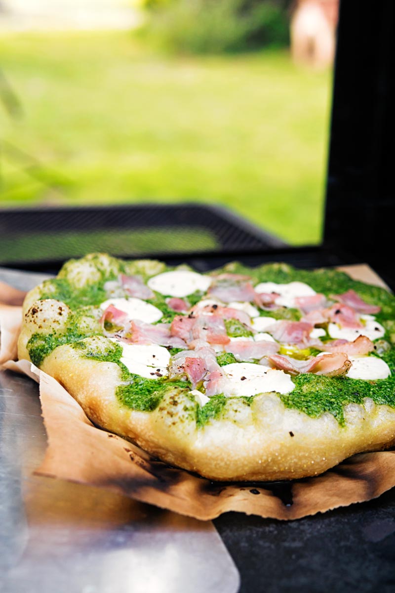 Portrait image of a Rocket Pesto Pizza with goats cheese and bacon cooked on a BBQ