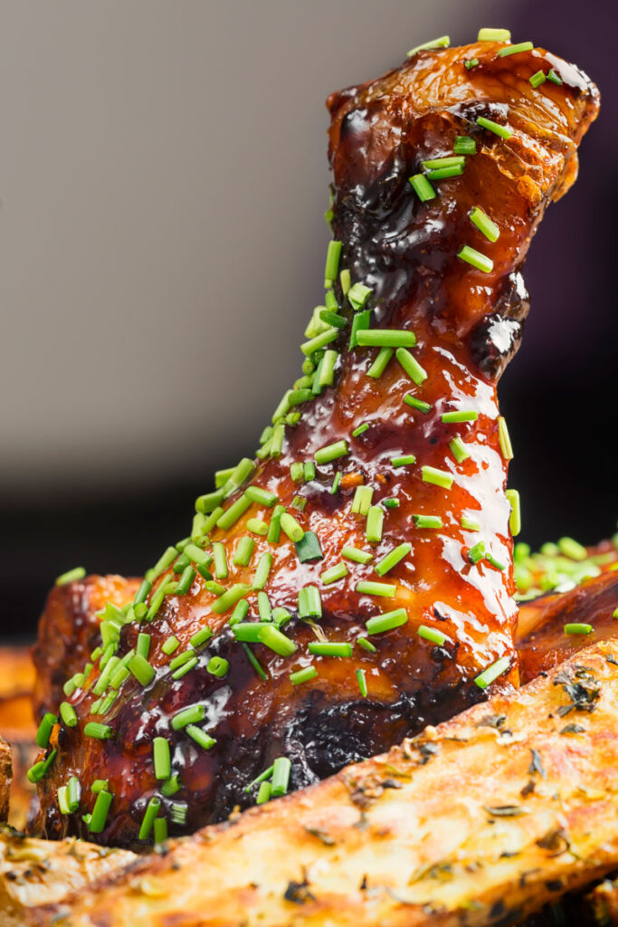 Portrait close up image of a sticky chicken drumstick with snipped chives