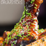 Portrait close up image of a sticky chicken drumstick with snipped chives with text
