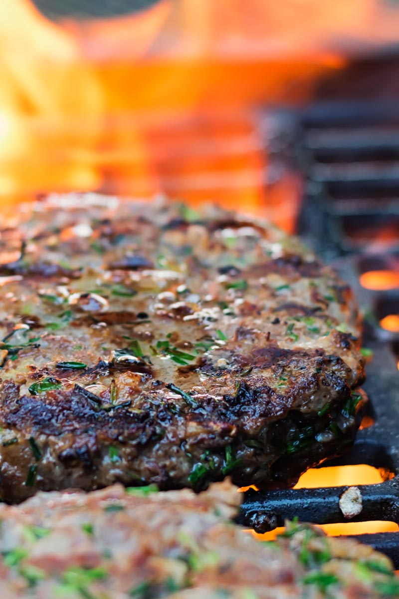 Portrait image of venison burgers cooking on a BBQ with a flame