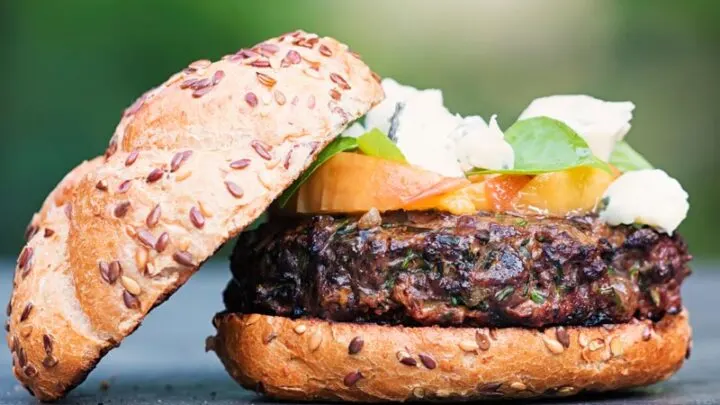 Landscape image of a venison burger with the top removed showing the peach, blue cheese and basil garnish