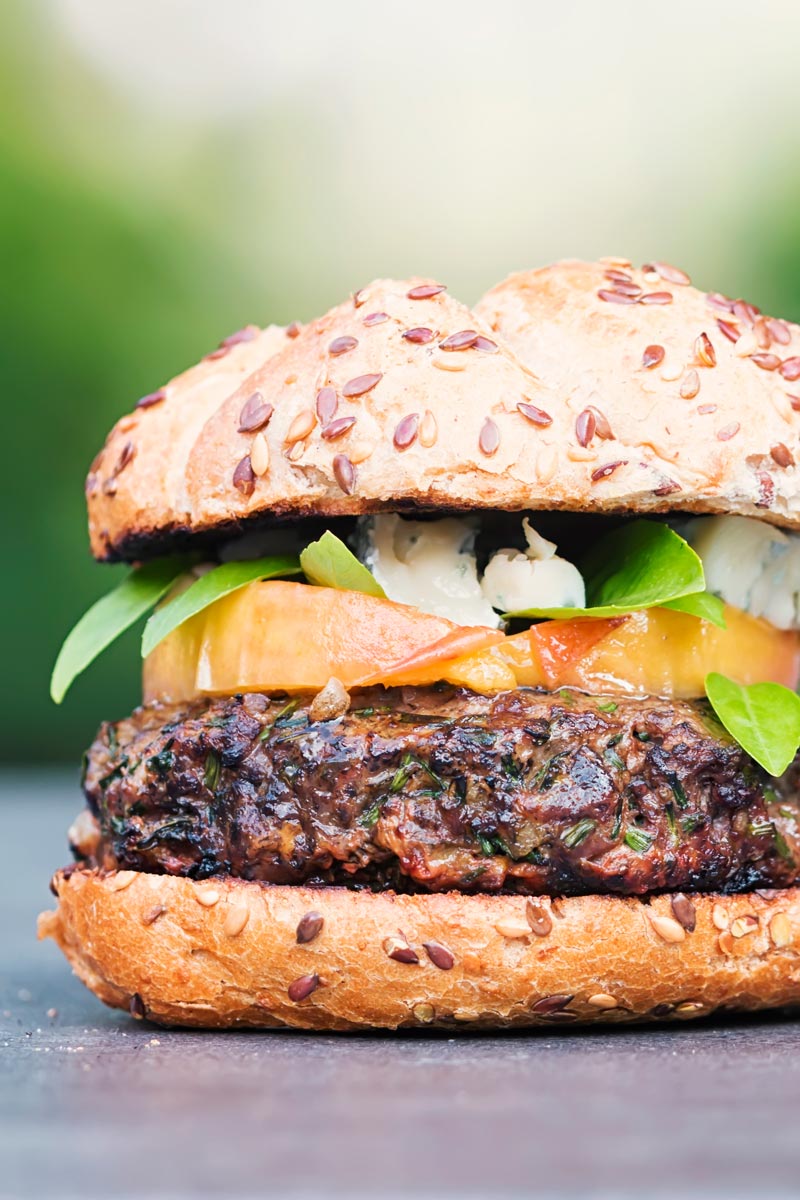 Portrait image of a venison burger with a peach, blue cheese and basil garnish