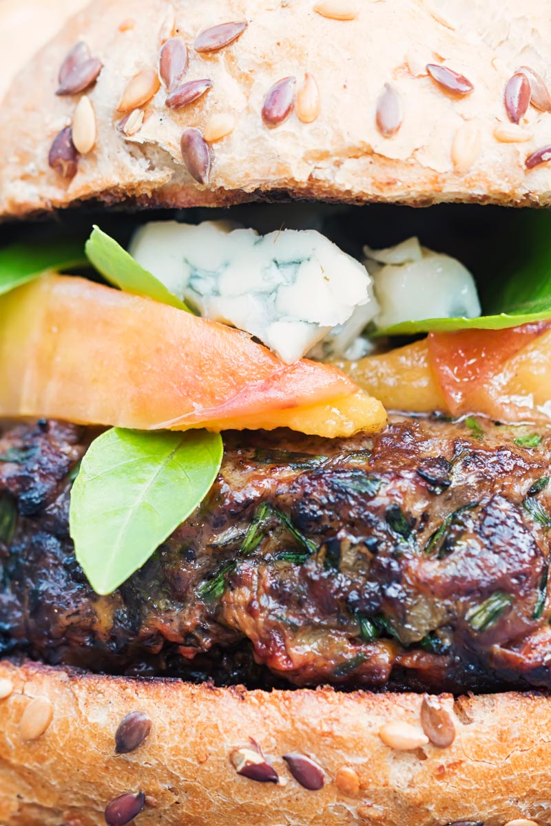 Portrait close up image of a venison burger with a peach, blue cheese and basil garnish