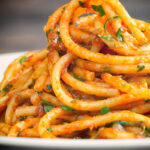 Portrait image of Bucatini pasta in a Puttanesca sauce with text overlay
