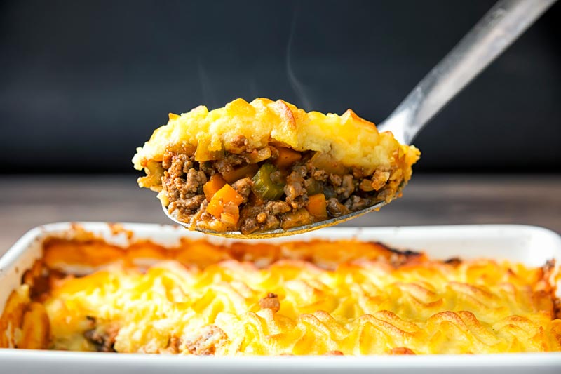 Landscape image of a serving spoon full of shepherds pie taken form a pie dish
