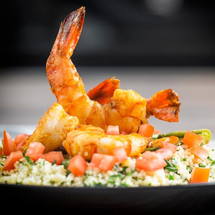 Square image of harissa garlic prawns served on a bed of buttered couscous